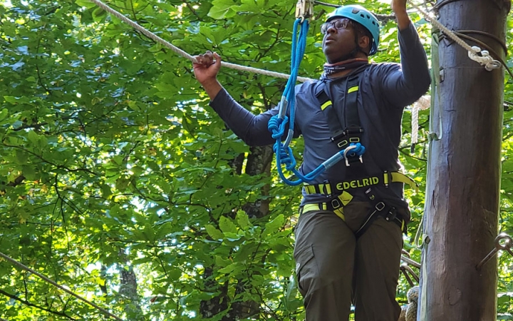 a person wearing rock climbing gear navigates a ropes course
